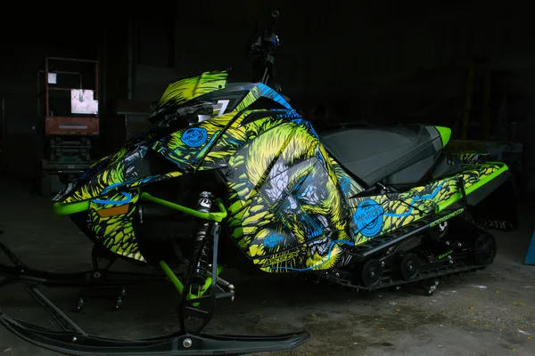 A Arctic Cat Next-Gen snowmobile with a black, blue, and lime squeeze Leif Alvarsson Tree Slayer custom vinyl wrap.