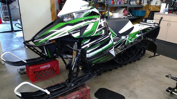 A Arctic Cat Procross snowmobile with a green, white and black stripes Bred2Win custom vinyl wrap.