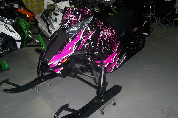 A Arctic Cat Procross snowmobile with a pink, white and black lightning Shock Treatment custom vinyl wrap.