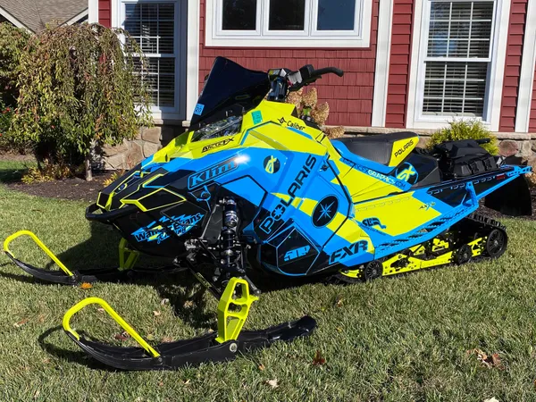 A Polaris Axys Crossover snowmobile with a lime squeeze, black, and blue Curtis Ascent custom vinyl wrap.