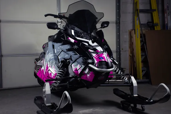 A Polaris Axys Trail snowmobile with a pink, black, and white Absolute Zero custom vinyl wrap.