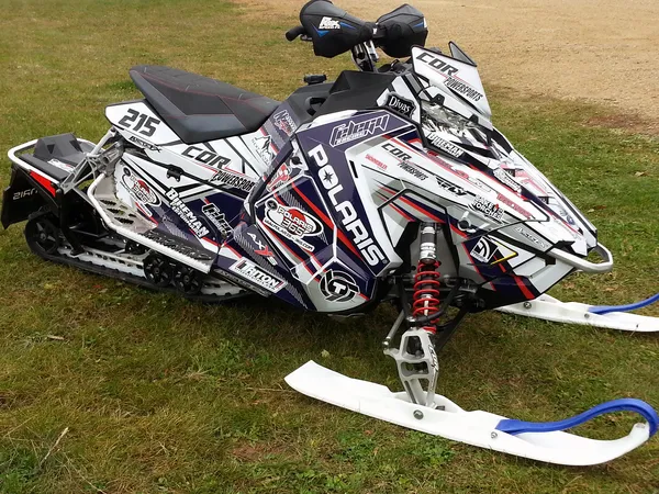 A Polaris Axys Trail snowmobile with a red, retro blue, and white Bred2Win custom vinyl wrap.