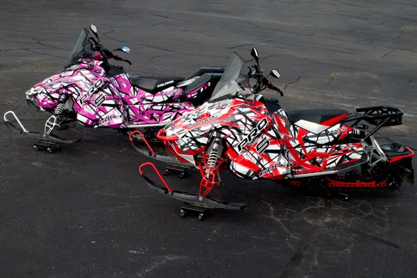 Two Polaris Axys Trail snowmobiles with black, white, red, and pink stripes Shattered Illusion custom vinyl wraps.