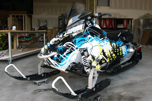A Polaris Axys Trail snowmobile with a black, blue, and lime squeeze Sub Zero custom vinyl wrap.