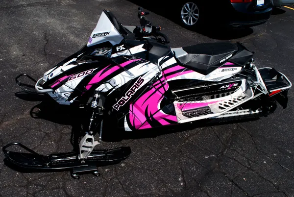 A Polaris Axys Trail snowmobile with a black, pink, gray, and white Surge custom vinyl wrap.