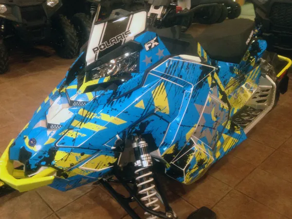 A Polaris Axys Trail snowmobile with a black, blue, and lime squeeze Wartorn custom vinyl wrap.