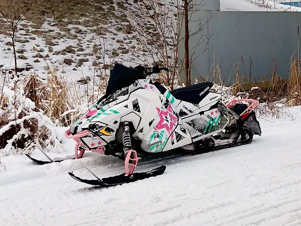 A Polaris Axys Trail snowmobile with a aqua, pink, and black Wartorn custom vinyl wrap.