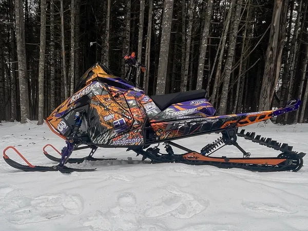 A Polaris Matryx Mountain snowmobile with a chrome, black, orange, and purple Leif Alvarsson Specter custom vinyl wrap.