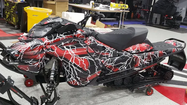 A Ski-Doo Gen4 Wide Body snowmobile with a red, white, and black Hard Rain custom vinyl wrap.