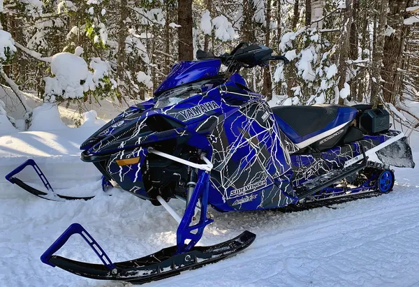 A Yamaha Sidewinder snowmobile with a blue, black, and white lightning Hard Rain custom vinyl wrap.