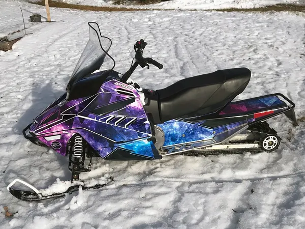 A Yamaha SnoScoot youth snowmobile with a black, purple, and blue galaxy Cosmic Camo custom vinyl wrap.